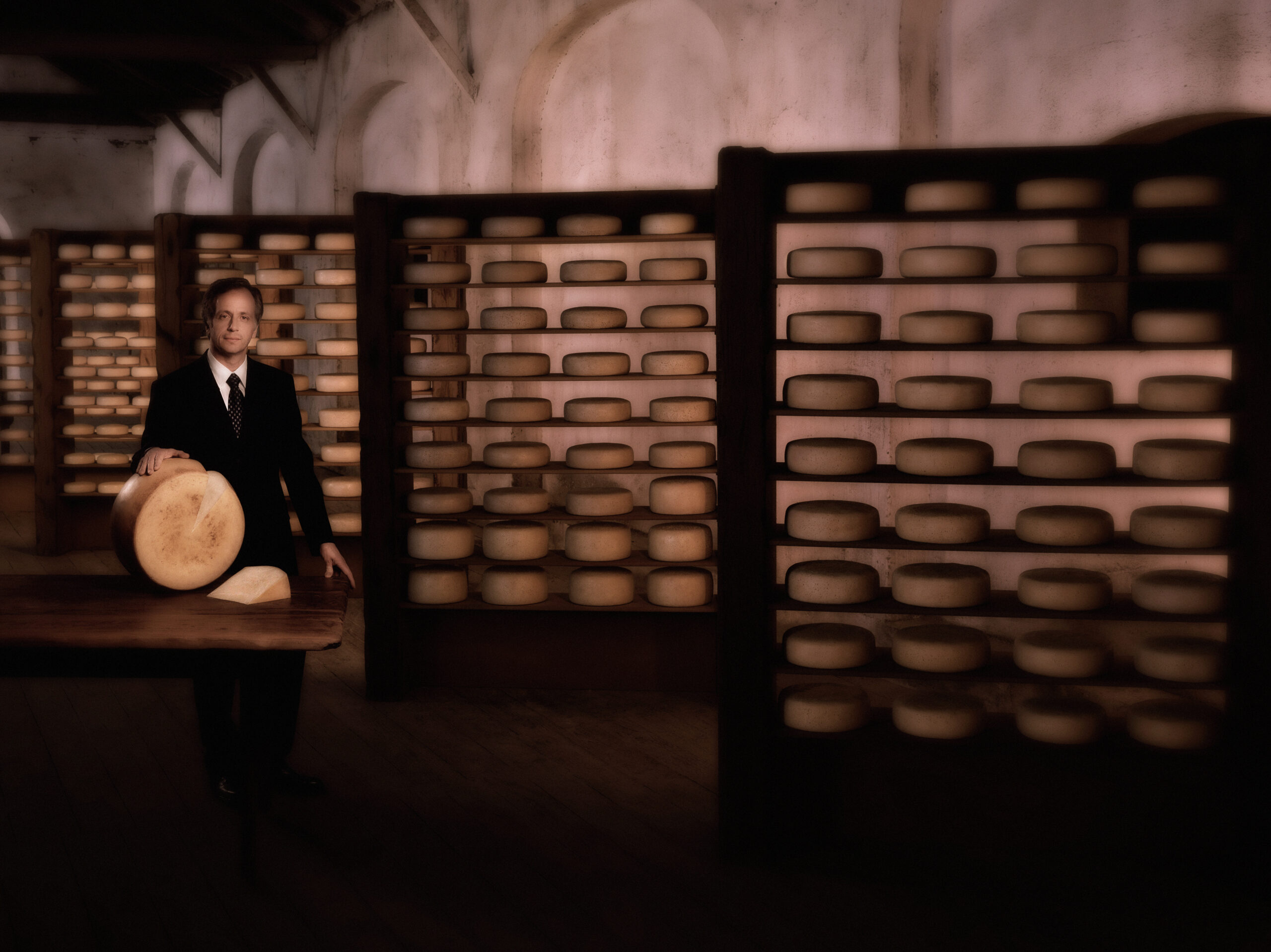 man with cheese round and background of stored cheese