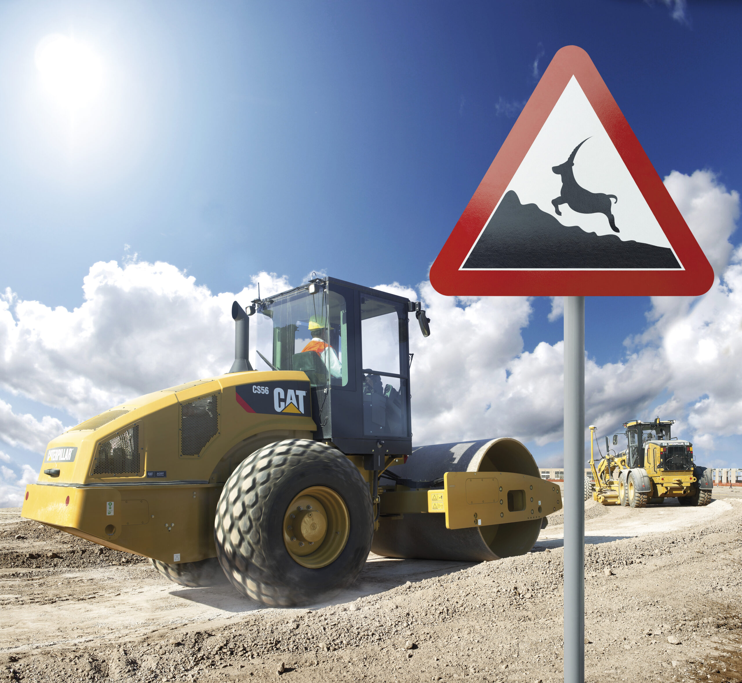 Road sign with antelope on mountain with Caterpillar soil compactor in background on rough road