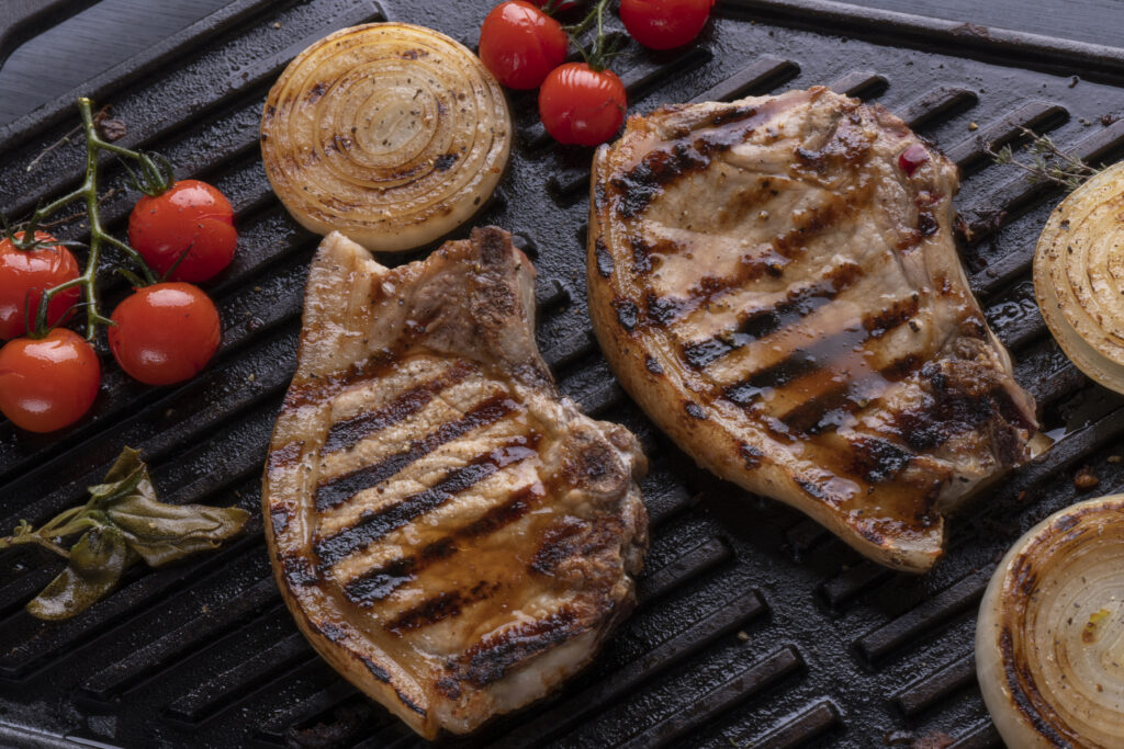Pork chops on Griddle with sear maks and cooking tomatoes and onion