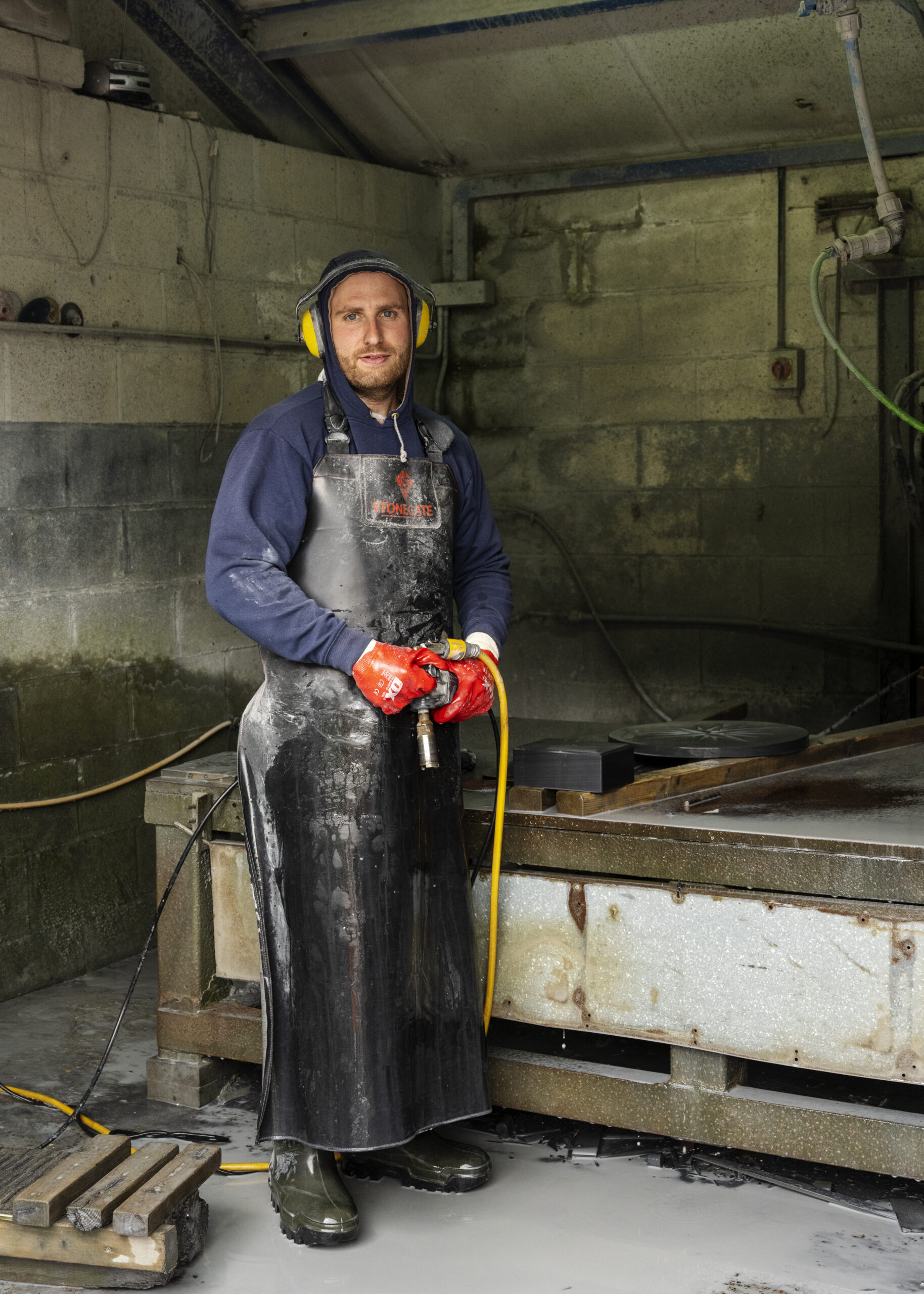 man in industrial space with ear defenders and protective apron looking to camera