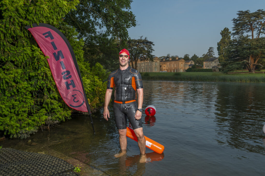 Man in wetsuit and goggles leaving water with Compton Verney house in background